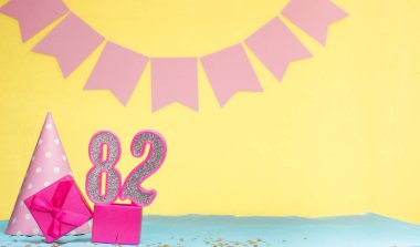 82 yaşında bir kızın doğum tarihi. Uzayı kopyala Sarı arkaplanlı pembe gözlüklü bir doğum günü. Üzerinde numaralandırılmış mumlar ve hediye kutusu olan dekorasyonlar. Bir kadın için yıldönümü kartı