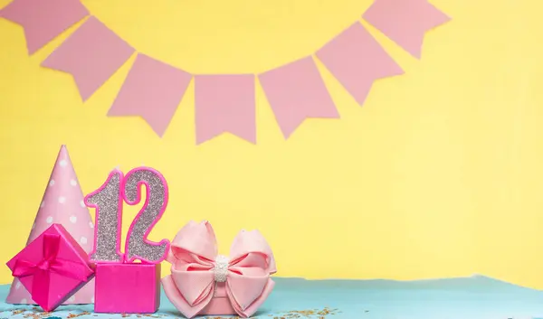 Date of birth for a girl  12. Copy space. Birthday in pink shades with a yellow background. Decorations with numbered candles and a gift box. Anniversary card for a woman