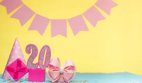 Date of birth for a girl  20. Copy space. Birthday in pink shades with a yellow background. Decorations with numbered candles and a gift box. Anniversary card for a woman