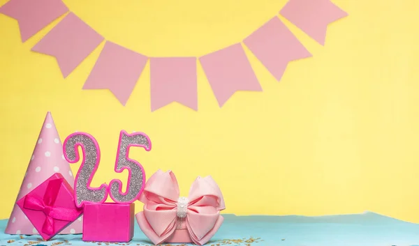 Date of birth for a girl  25. Copy space. Birthday in pink shades with a yellow background. Decorations with numbered candles and a gift box. Anniversary card for a woman