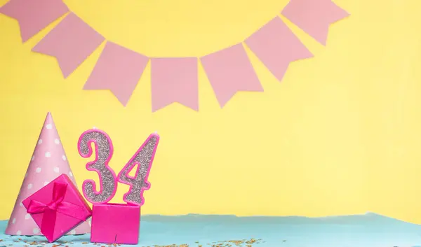 Date of birth for a girl  34. Copy space. Birthday in pink shades with a yellow background. Decorations with numbered candles and a gift box. Anniversary card for a woman