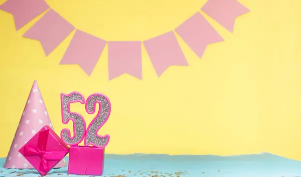 Date of birth for a girl  52. Copy space. Birthday in pink shades with a yellow background. Decorations with numbered candles and a gift box. Anniversary card for a woman