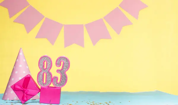 Date of birth for a girl  83. Copy space. Birthday in pink shades with a yellow background. Decorations with numbered candles and a gift box. Anniversary card for a woman