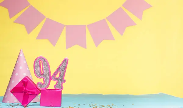 Date of birth for a girl  94. Copy space. Birthday in pink shades with a yellow background. Decorations with numbered candles and a gift box. Anniversary card for a woman