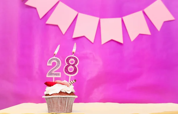 Background date of birth with number  28. Pink background with a cake and burning candles, save space, happy birthday anniversary for a girl. Holiday pudding muffin.