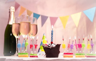 Şampanya ve bardaklarla doğum günü. Doğum günü mumu, kek ya da kek ile. Yıldönümü kartı ve çelenkler yer açıyor. Neşeli arkaplan.
