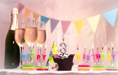 Şampanya ve bardaklarla doğum günü. 3 numaralı doğum günü mumu. Yıldönümü kartı ve çelenkler yer açıyor. Neşeli arkaplan.