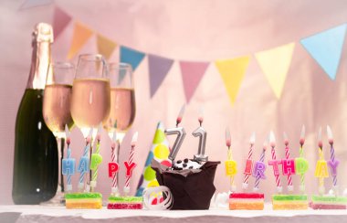 Şampanya ve bardaklarla doğum günü. 71 numaralı doğum günü mumu. Yıldönümü kartı ve çelenkler yer açıyor. Neşeli arkaplan.