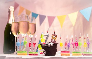 Şampanya ve bardaklarla doğum günü. 78 numaralı doğum günü mumu. Yıldönümü kartı ve çelenkler yer açıyor. Neşeli arkaplan.