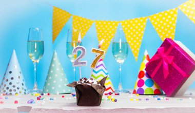 Doğum günü kutulu bir kadın ya da kız için doğum tarihi. Mum sayısı 27 olan turta. Yıldönümü kartı ve şampanya. Tatil süslemeleri. Mutlu yıllar.