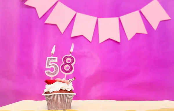 Background date of birth with number  58. Pink background with a cake and burning candles, save space, happy birthday anniversary for a girl. Holiday pudding muffin.