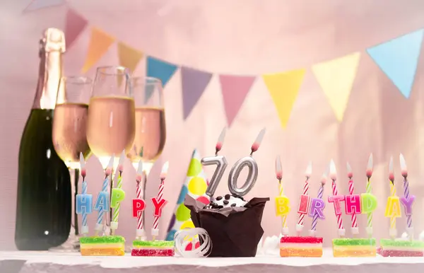 Şampanya ve bardaklarla doğum günü. 70 numaralı doğum günü mumu. Yıldönümü kartı ve çelenkler yer açıyor. Neşeli arkaplan.