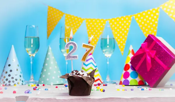 Doğum günü kutulu bir kadın ya da kız için doğum tarihi. Mum sayısı 27 olan turta. Yıldönümü kartı ve şampanya. Tatil süslemeleri. Mutlu yıllar.