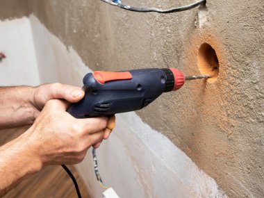 Tuğla duvarda bir priz için bir delik açmak, priz için bir matkap, elektrik tamiratı yapan bir işçi, duvardaki elektrik kabloları...