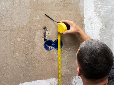 Duvara bir kutu soketi yerleştirmek, bir elektrikçi prizleri takmak, elinde mezura olan profesyonel bir tamirci....