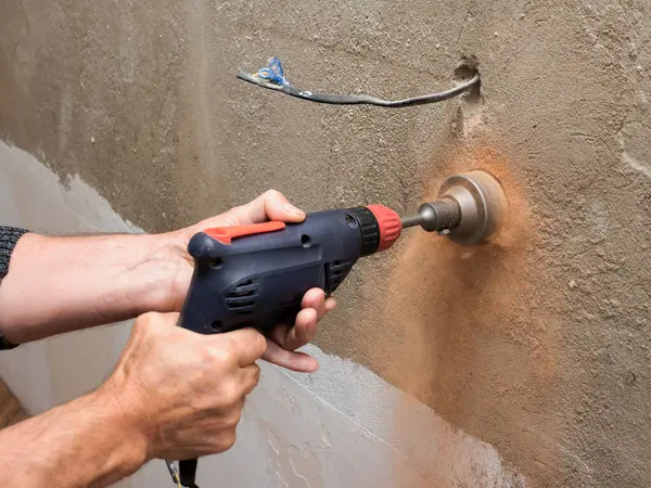 Drilling a socket in a brick wall, a drill for a socket, a worker doing electrical repairs