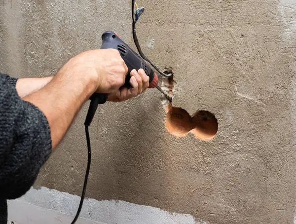 Drilling a hole for an outlet in a brick wall, a drill for an outlet, a worker doing electrical repairs, electrical wiring in the wall