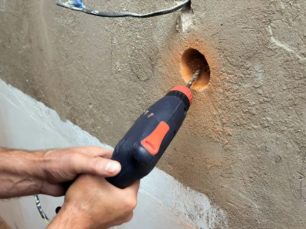 Drilling a socket in a brick wall, a drill for a socket, a worker doing electrical repairs, electrical wiring in the wall