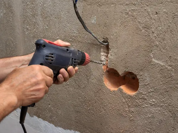 Drilling a hole for an outlet in a brick wall, a drill for an outlet, a worker doing electrical repairs, electrical wiring in the wall