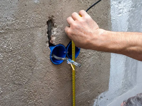 Installation of a box socket in the wall, an electrician installs sockets, a professional handyman installer with a tape measure in his hands.