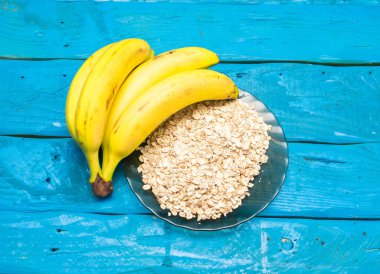 Kahvaltı, yulaf ezmeli muz ve bardakta taze süt. Mavi tahtada, olgun muzlar mavi ahşap bir masada.