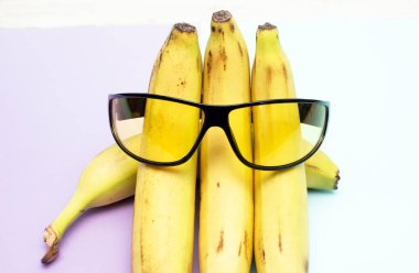 Koyu güneş gözlüklü muzların yaratıcı arka planı, üst görünüm, telif alanı. Çok renkli arkaplanda gözlüklü meyveler.