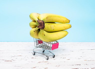 Mavi arka planda market sepeti içinde muzlar. Muzlar süpermarket arabasında.