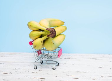 Mavi arka planda market sepeti içinde muzlar. Muzlar süpermarket arabasında.