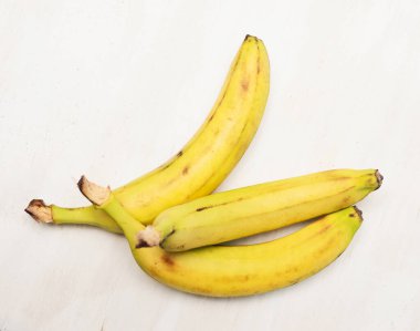 Üç olgun muz, ahşap mutfak masasının üstünde.