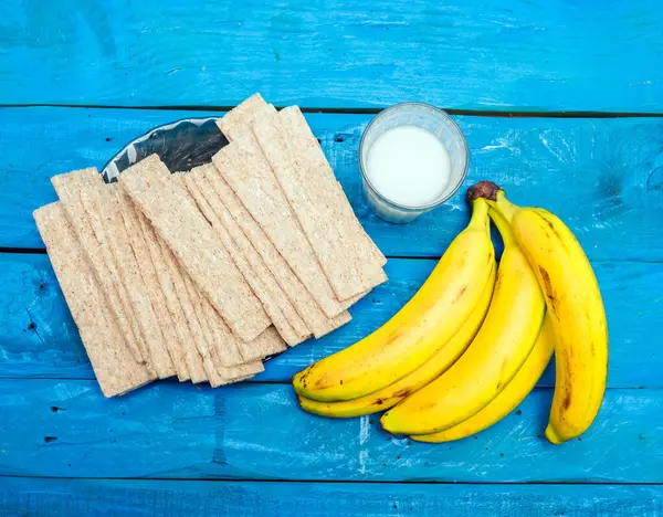 Dry bread with milk and banana for morning breakfast. A glass of milk with a banana with crackers, on a wooden kitchen table.