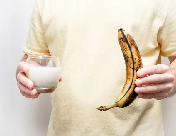 A banana in the peel of a man\'s hand. Hold a banana with a glass of milk or yogurt in your hands.