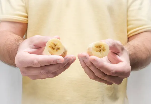 A man holds a sliced banana in his hands. Keep bananas in pieces without peel.