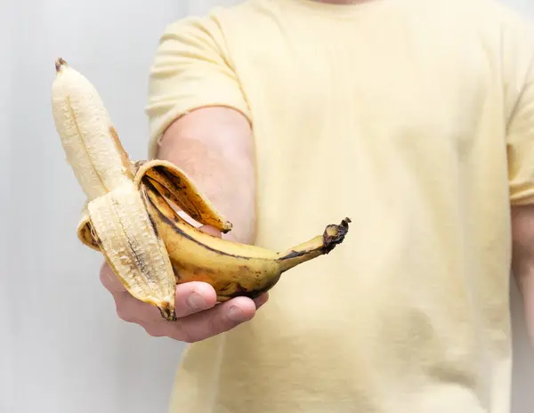 A banana is in the hands of a man without a peel. Holding bananas in a man\'s strong hand