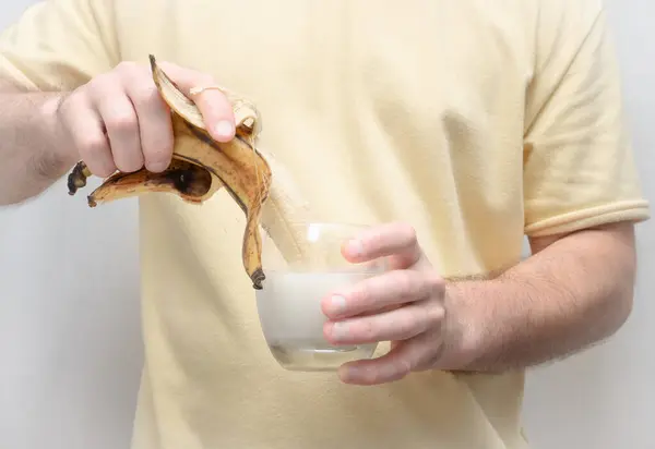 A man holds a banana without a peel with a glass of fresh milk or yogurt. Holding bananas in a man\'s strong hand