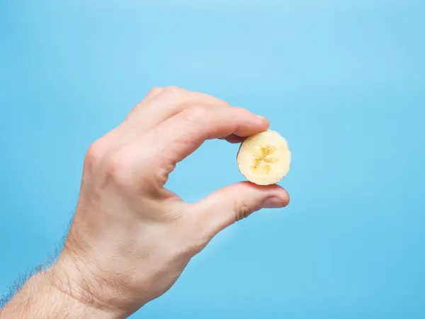 A man holds a piece of banana without a peel in his hand, copyspace.