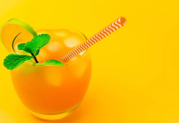 Lemonade with a straw in a glass. Summer drink orange with mint, with ice. Soda in a transparent glass. Apperol alcoholic drink, on a yellow background, close-up.