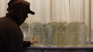 Bir adam dairesinde şişe su bulundurur. Bir adam kilerini su şişeleriyle dolduruyor. İçki eksikliği. Acil su kaynağı.
