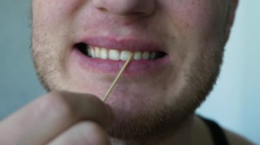 Bir adam dişlerini kürdanla fırçalar, dişlerinin arasını tahta bir bambu kürdanla temizler. Diş bakımı