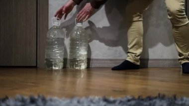 Adam plastik şişelerde acil durum suyu depoluyor. Su sıkıntısı çekiyor. Elinde bir şişe su olan bir adam.
