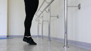 Balerin salonda ısınıyor. Bale barında ayakta duran bir balerin ayaklarını esnetir. Bale ayakkabılı ayaklar.