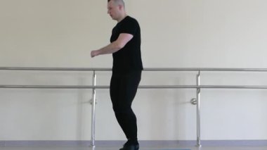Bir dansçı antrenman sırasında zıplama yapar. Erkek dansçı ısınıyor. Spor salonunda jimnastik paspasının üzerinde.