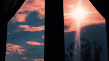 Evin penceresinden gün batımı manzarası. Güçlü bir rüzgar pencerenin dışındaki ağacı sallar. Bulutlu güzel pembe gökyüzü