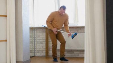 Genç bir adam temizlik için süpürgeyle dans eder, neşeli bir adam evde müzik dinler ve dans eder. Yaşam biçimi