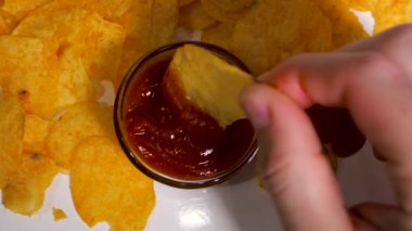 Ellerinle kırmızı soslu patates cipsi yiyorsun, yakından, yavaş çekimde.