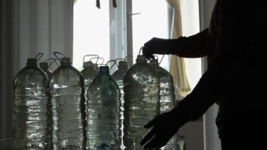 Elinde bir şişe içme suyu olan bir adam, kamera yavaş çekim. Evde az miktarda içme suyu var..