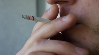 Genç bir adam sigara içiyor. Tütün dumanı soluyor. Sigara içme odasında tütün içmek, yakın plan.