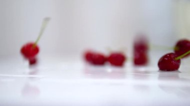 Yumuşak odaklı kamera, olgun kiraz çileği beyaz bir masaya yavaş çekimde güzel bir şekilde düşer. Sonbaharda beyaz arka planda kiraz üzümü
