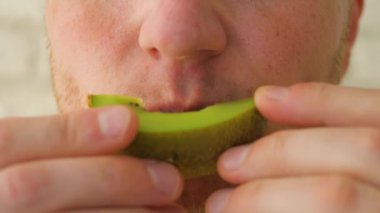 Genç adam kivi meyvesi yiyor, ağır çekimde. Yakın plan.