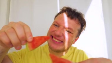 Elinde karpuzla gülümseyen neşeli bir adam. Ağır çekim. Genç bir adamın ellerinde bir karpuz dilimi.