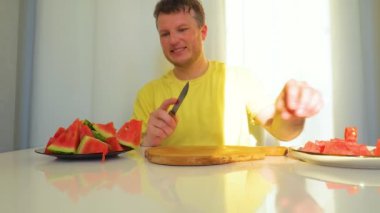 Adamın biri apartmandaki mutfak masasında karpuz kesiyor. Yavaş çekim.